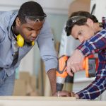 carpenter and carpenter’s assistant drilling wood